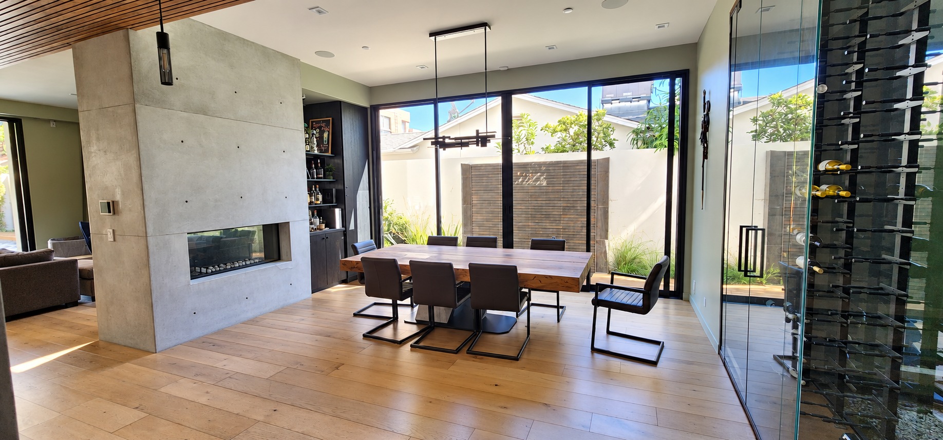 Hartsook dining room with a concrete fireplace, wood dining table, pendant light, and glass wine display