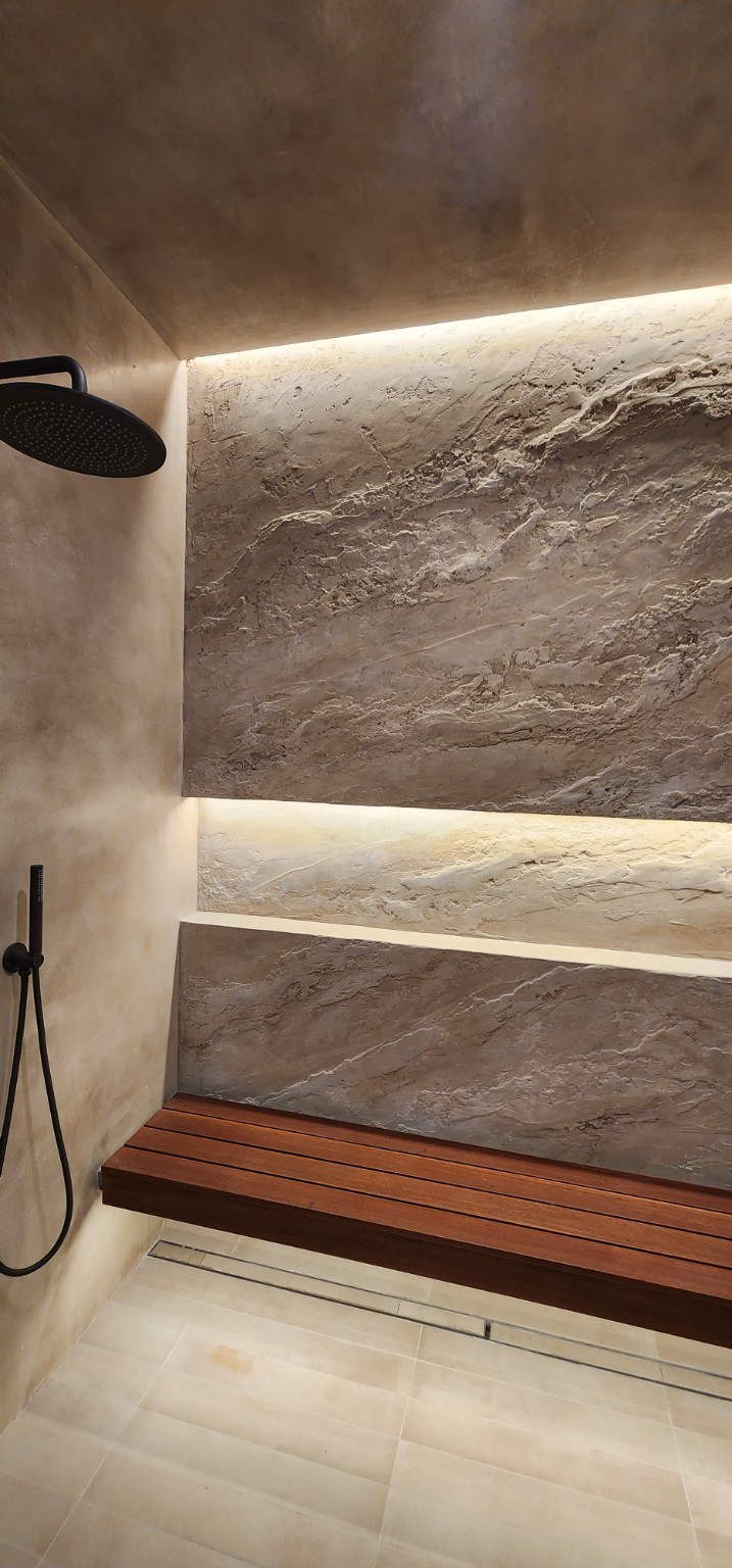 Shower with textured wall panels, concealed lighting, black fixtures, and a wood bench