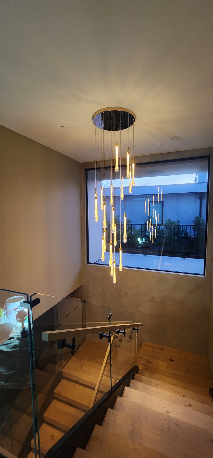 Wood staircase with glass railing beneath a cascading pendant chandelier